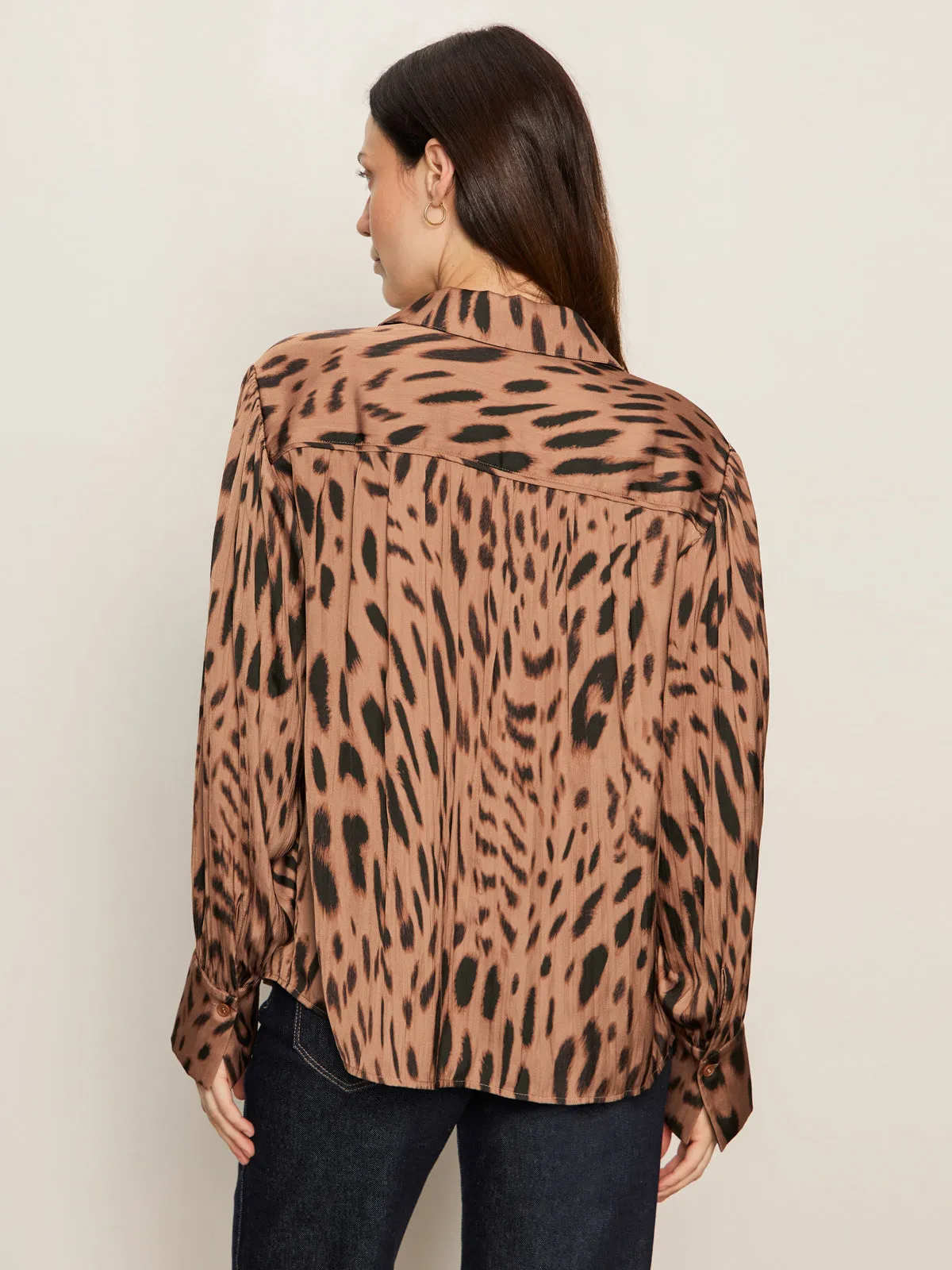 A woman with long brown hair, seen from behind, wears the Sanctuary Clothing "colette shirt mocha leo," a loose-fitting, long-sleeve brown and black animal print top, paired with dark jeans against a plain light background.