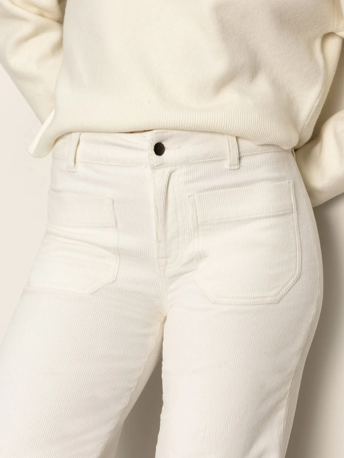 A person wearing Sanctuary Clothing's corduroy marine pant in chalk, featuring front patch pockets, paired with a matching off-white sweater, shown from waist to mid-thigh.