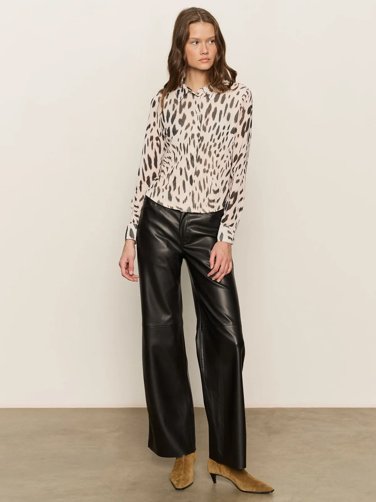 A woman with wavy brown hair and a neutral expression wears the Sanctuary Clothing fitted mesh button down top mother leo??a long-sleeved animal print blouse??against a plain background. She pairs it with black wide-leg leather pants and tan pointed-toe an