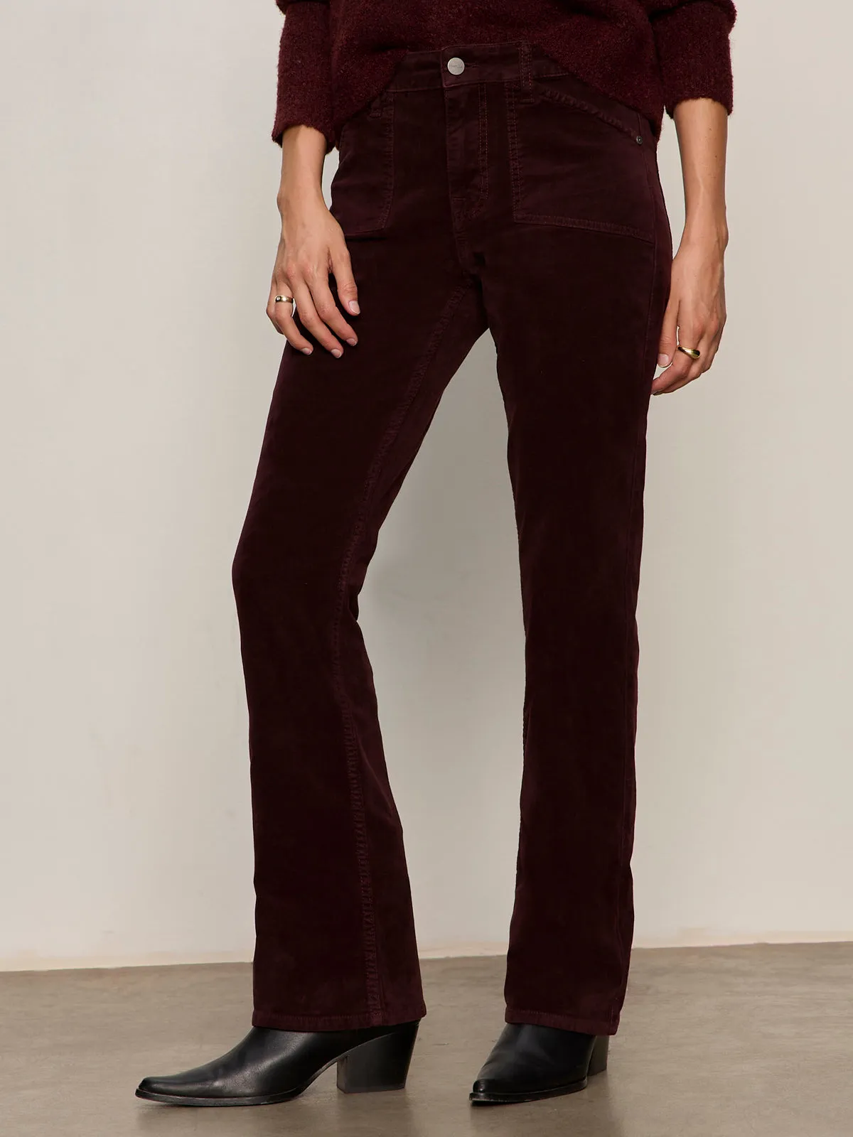 A person wearing Sanctuary Clothing's velveteen brook bootcut pant in dark crimson (petite), paired with a matching top and black heeled boots, stands against a neutral background. Only the lower half of the body is shown.