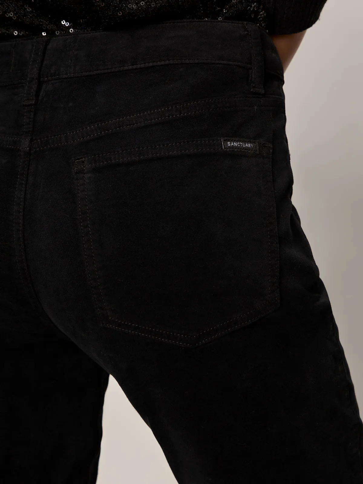 Close-up of the back pocket of velveteen brook bootcut pant in black petites by Sanctuary Clothing, showing a small brand tag above the pocket being worn.