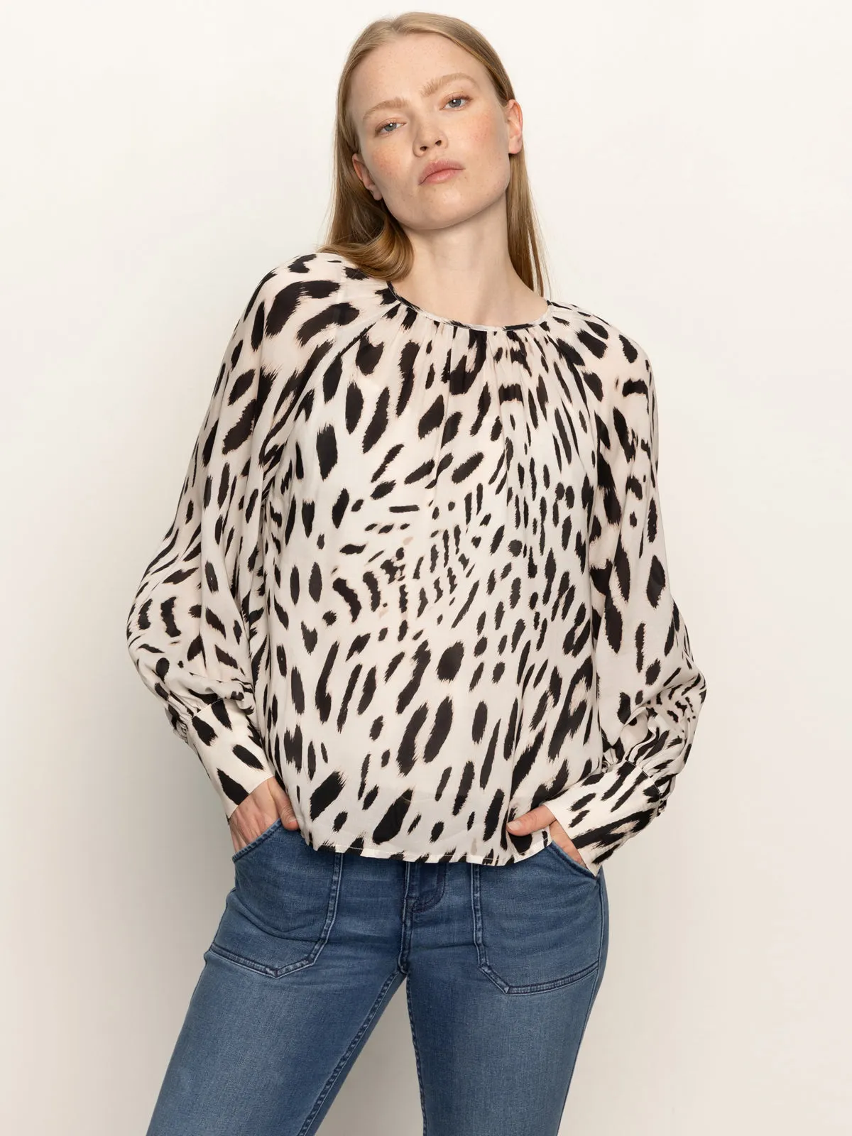 A woman with long blonde hair wears the Sanctuary Clothing wild dreamer blouse mother leo, a loose-fitting, long-sleeve animal print top, with blue jeans and hands in her pockets against a plain light background.
