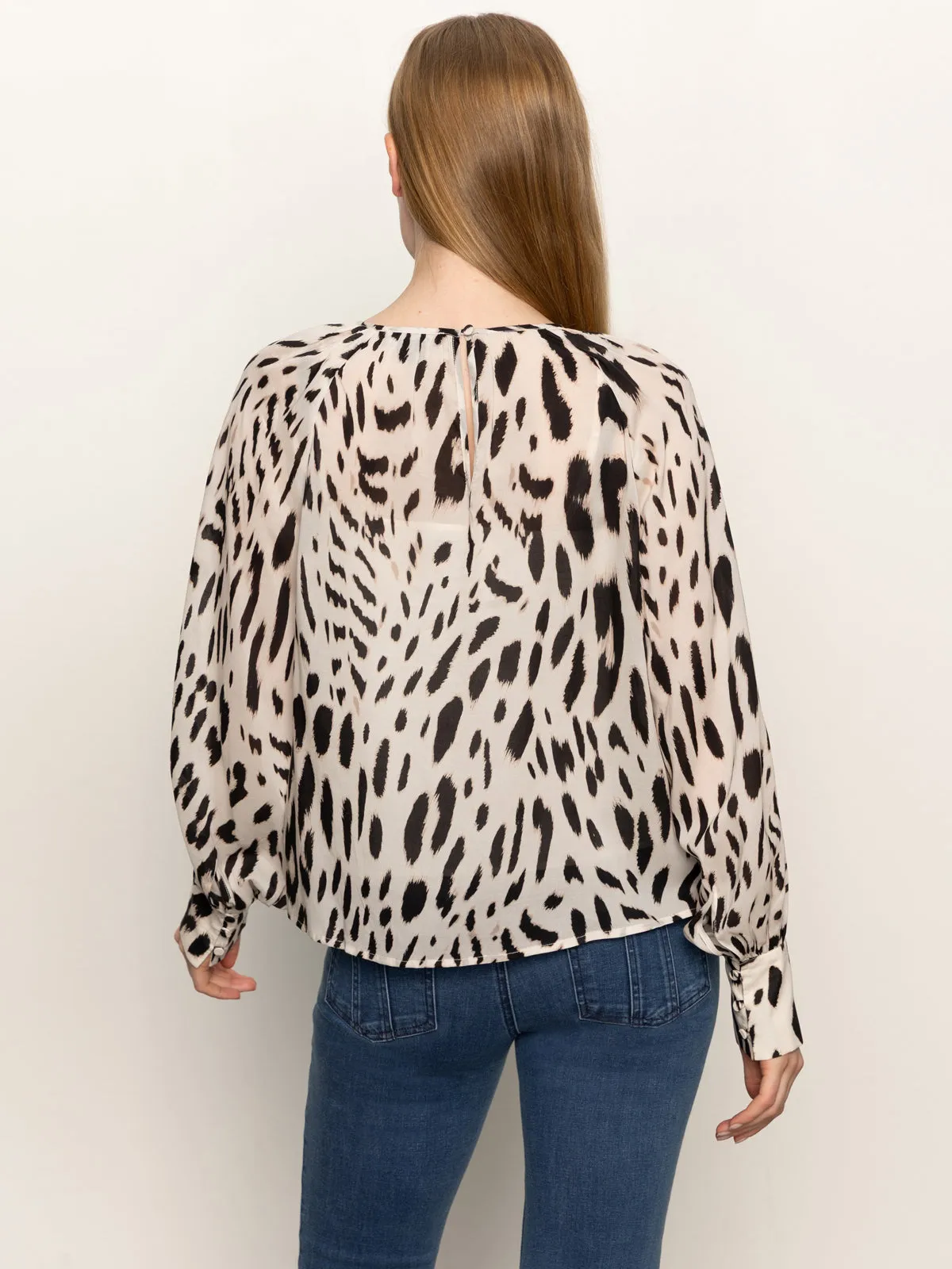 A person with long, straight brown hair is shown from the back, wearing Sanctuary Clothing??s wild dreamer blouse mother leo in a black and beige animal print and blue jeans.
